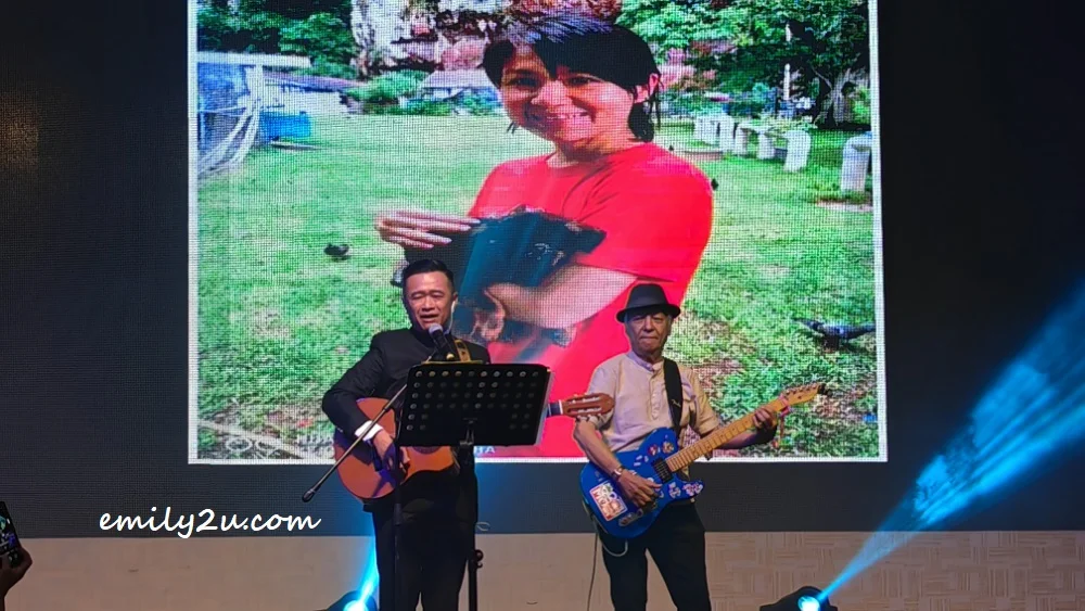 ISPCA Chairman Ricky Soong sings Take Me Home, Country Roads while strumming the guitar, accompanied by Kenny Ham (R)